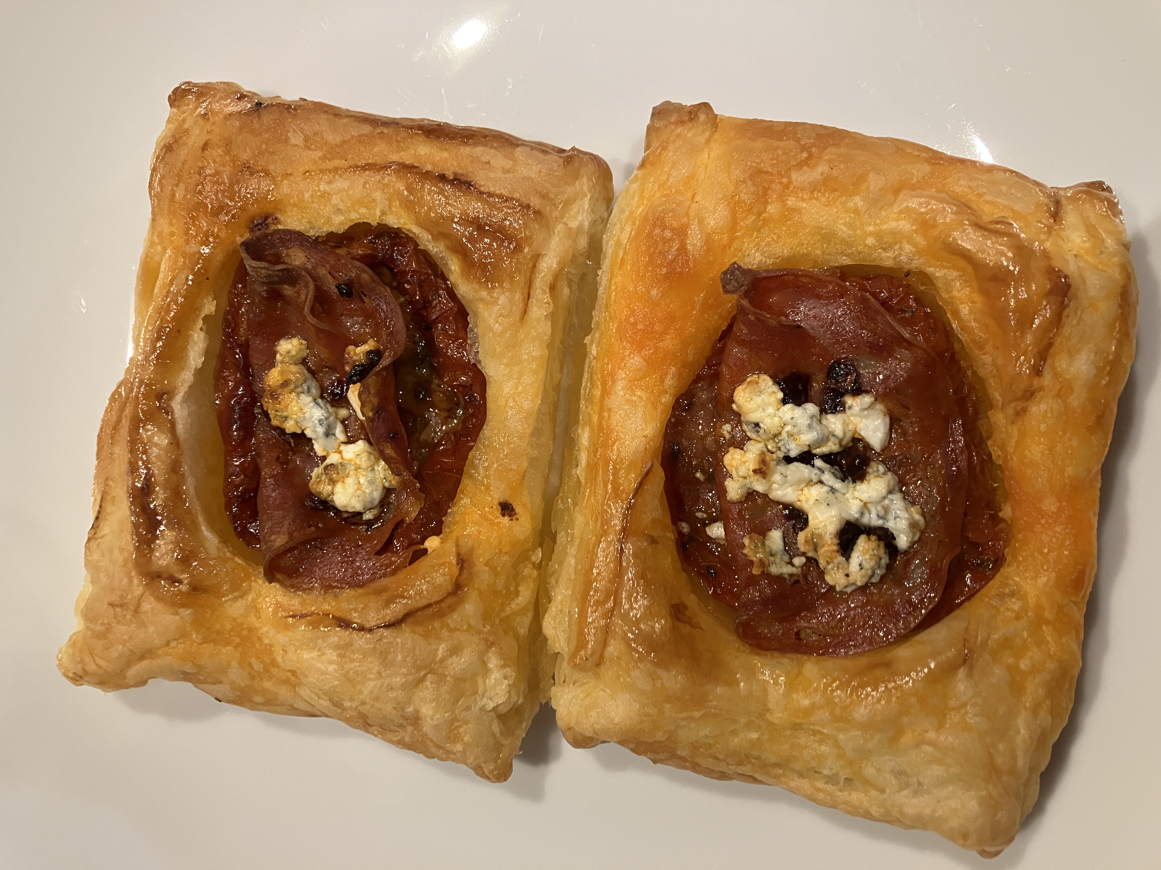 two pastry rectangles with sundried tomatoes, chorizo, and golden brown goats cheese in the middle, on a white plate