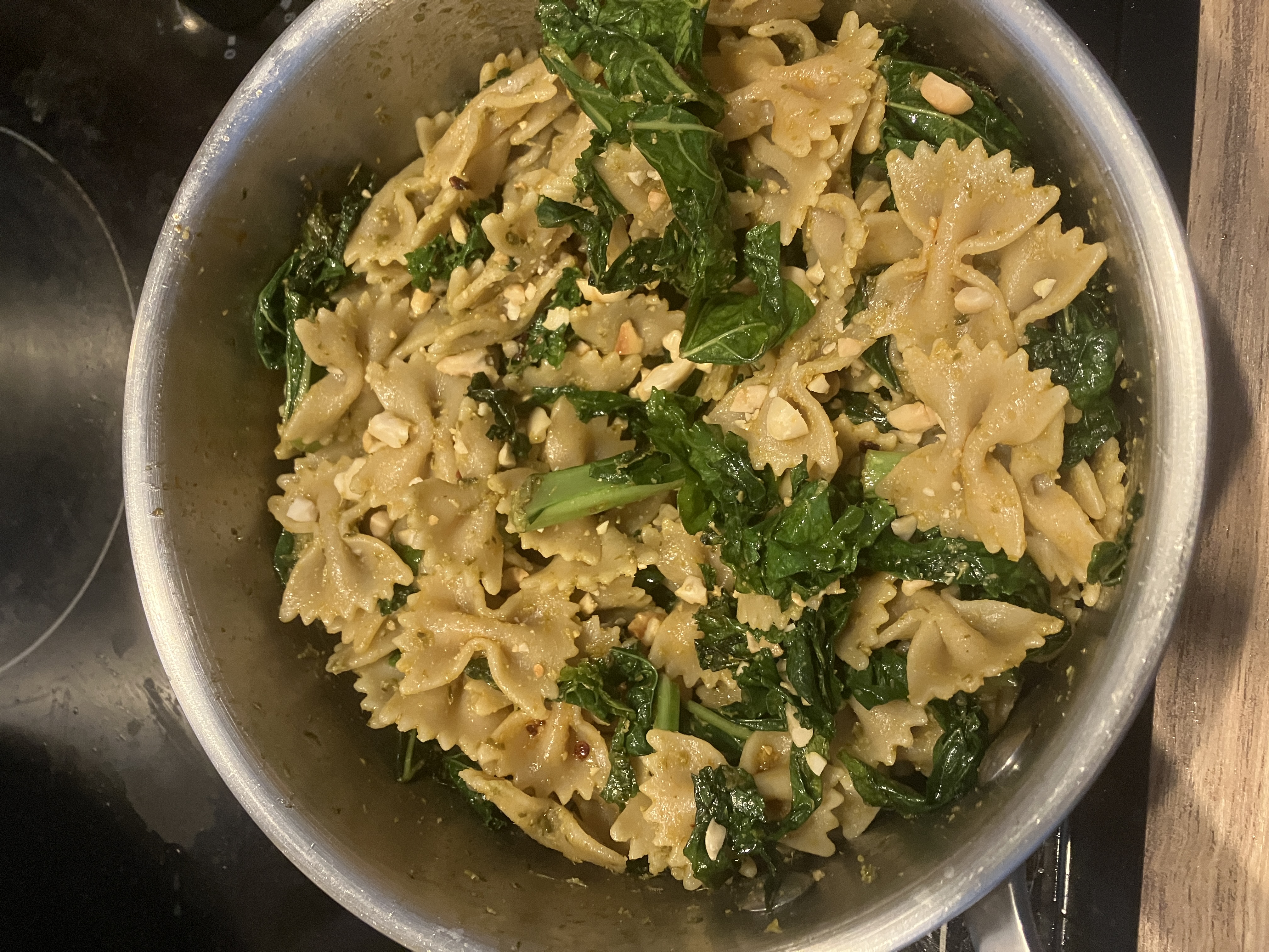 farfalle pasta, with cooked kale leaves, green pesto, chilli flakes and crushed peanuts in a saucepan