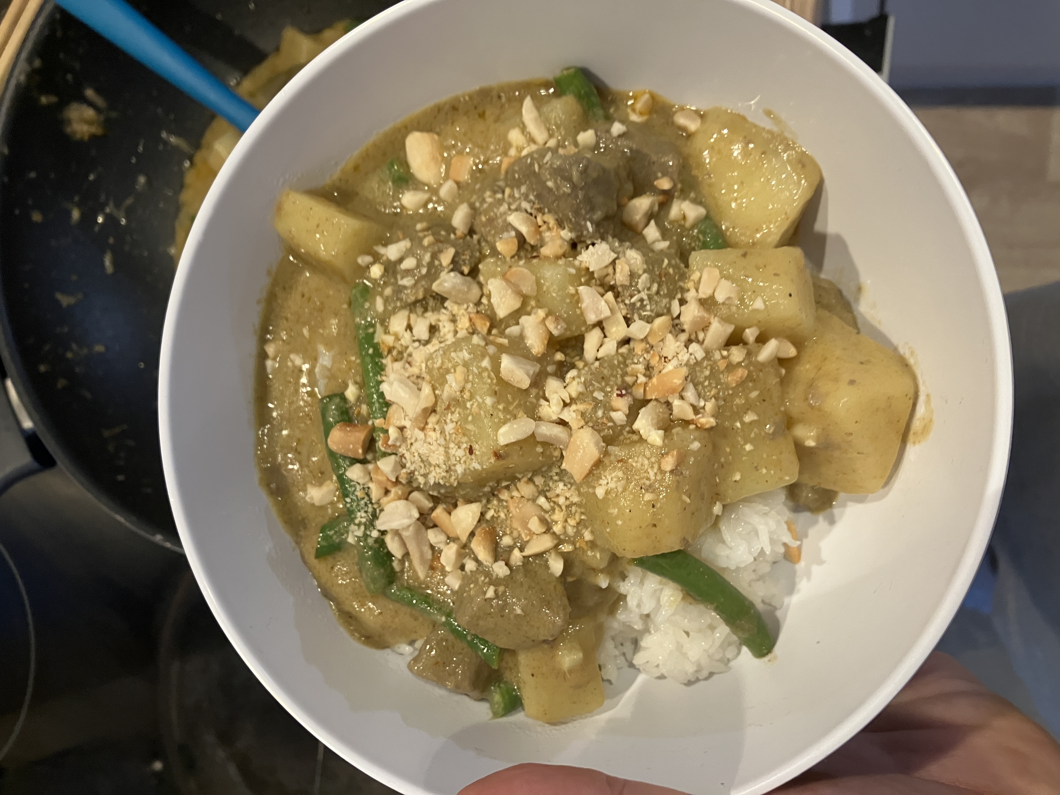 a bowl of yellow curry with potatoes, beef and green beans over rice. there are crushed peanuts sprinkled on top