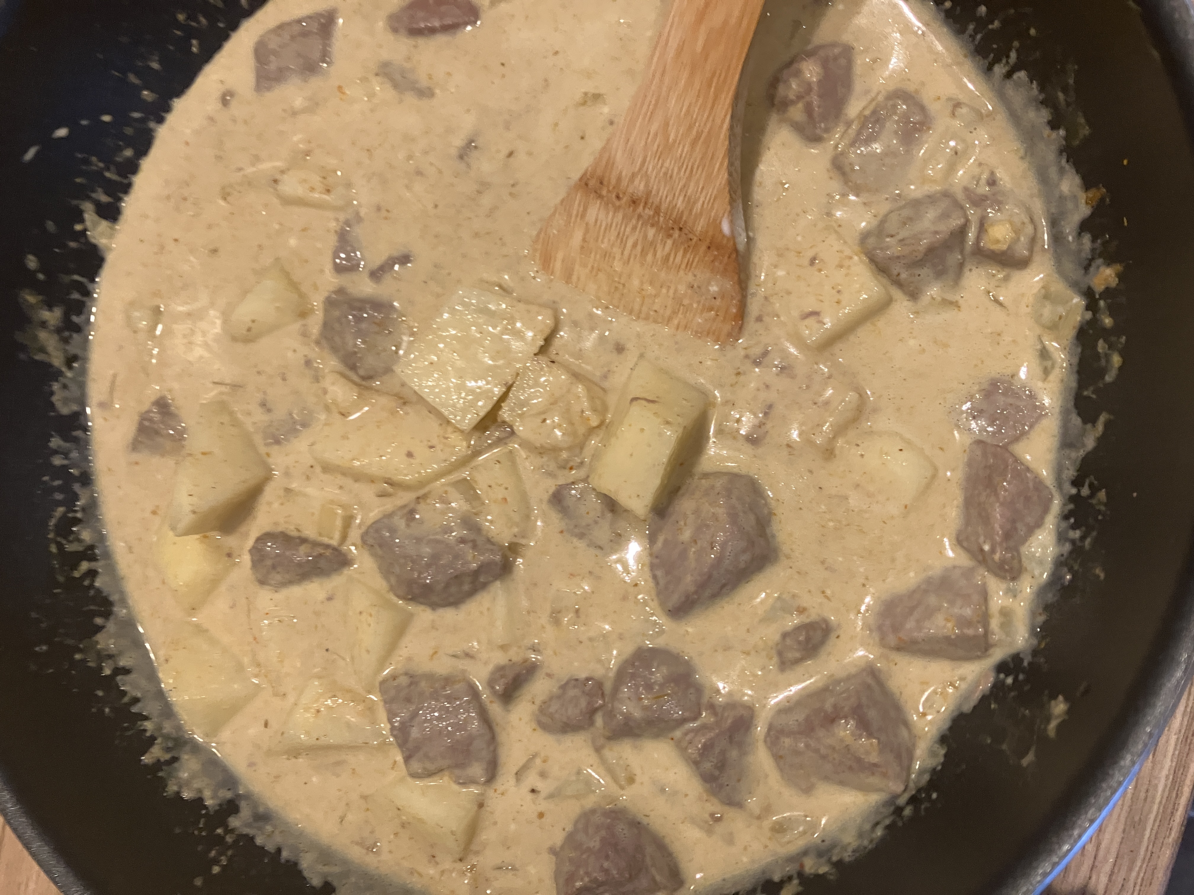 potatoes, beef and green beans in a pale-coloured curry in a wok